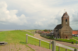 An old church in a Frisian village and a grass-covered sea dike on the left side