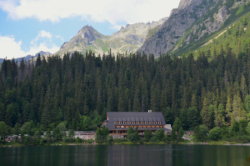 A mountain lake in the High Tatras with a large cottage, thick forest and mountains in the background