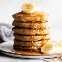 Banana cinnamon pancakes in a stack topped with slices of banana and maple syrup