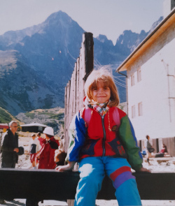 A young girl with short brown hair wearing colourful clothing pictured in front of a tall rocky mountain in the High Tatras