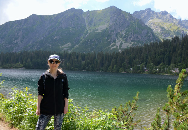 Young woman standing in front of a mountain lake with a forest and mountains in the background